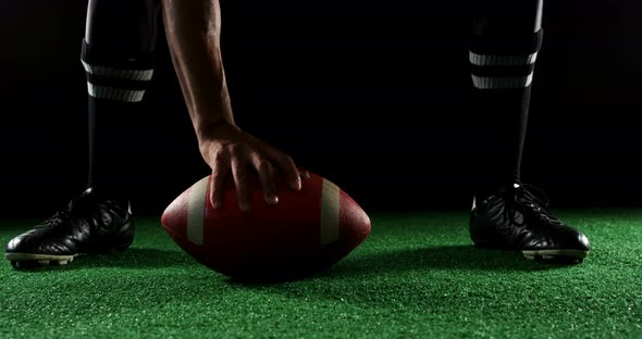 American football player bending holding a ball on turf with his hands alt