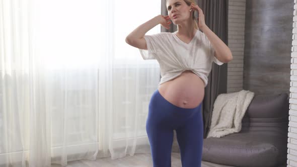 A Cheerful Pregnant Woman with a Big Tummy Dances to Music in Her Living Room She Does Exercises on