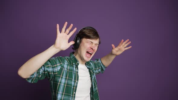 Emotional Man in Shirt Listening to Music on Headphones on Purple Background alt