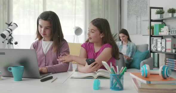 Cute happy girls doing their homework, they are connecting online and getting distracted