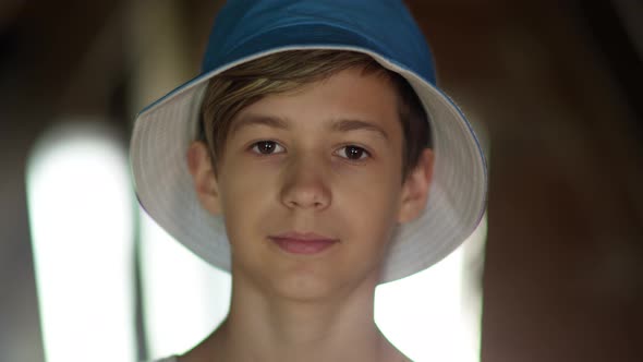 Portrait of a Happy Boy in a Blue Hat Looking at the Camera and Smiling Near the Window