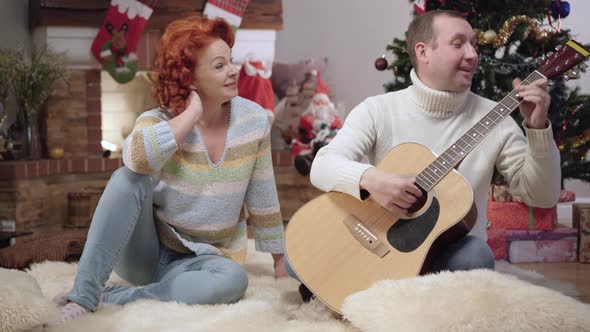Wide Shot Portrait of Happy Relaxed Caucasian Man and Woman Playing Guitar and Singing on Christmas alt