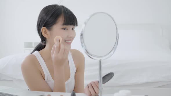 Beauty of young asian woman with learning makeup with powder puff on cheek watching laptop computer. alt
