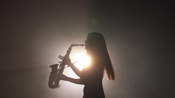 Young Beautiful Girl in a Dark Dress Plays on a Golden Shiny Saxophone on Stage alt