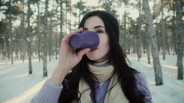 Positive Woman in Warm Sweater Drinks Tea in Winter Forest