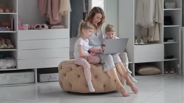 Young Mother with Her Twin Daughters Choose Things Online in Her Cozy Apartment