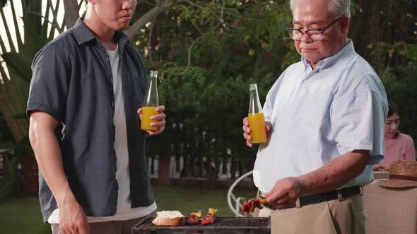 Happy Asian family having a barbecue-BBQ party together in the garden at home. alt