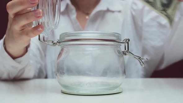 A Woman Puts a Banknote in a Jar alt