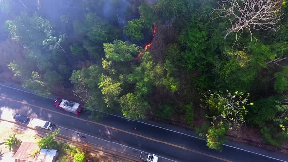 Aerial view of a firetruck at a tropical forest fire near a road and accommodation, in South America alt