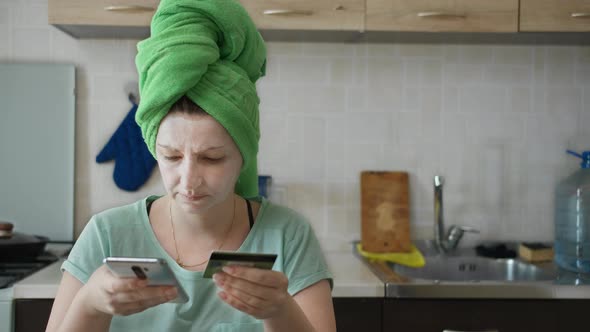 Woman Sits in the Kitchen and Shopping with Bank Card and Phone