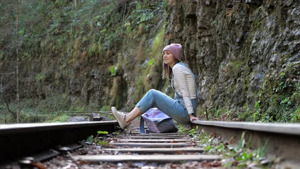 Young Backpacker Woman is Sitting on Train Rail and Resting Alone