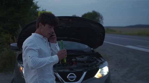 Drunk Man Stands Near His Broken Car on Road alt