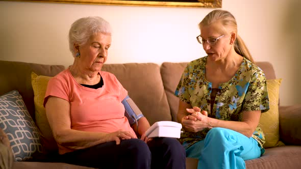 Home healthcare nurse and elderly woman taking blood pressure with a machine. alt