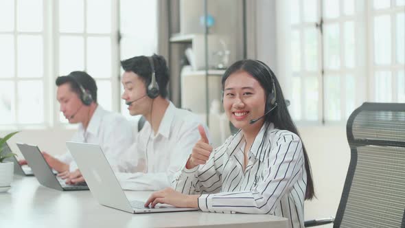 A Woman Of Three Asian Call Centre Agents Smile To Camera Then Thumbs Up alt