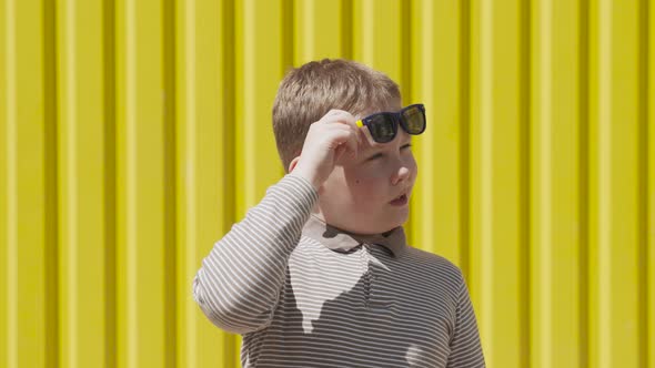 Boy Raises His Sunglasses and Looks Suspiciously Near Bright Yellow Ribbed Wall alt