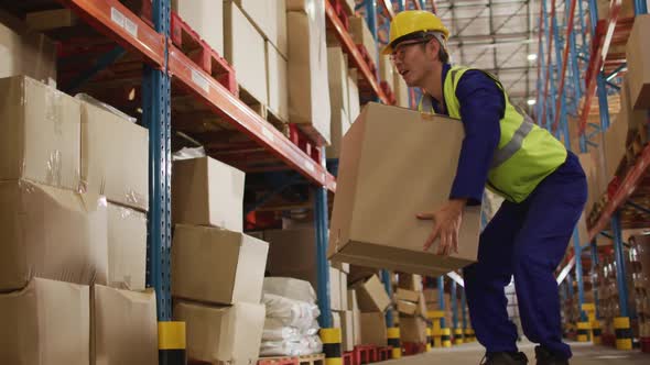 Asian male worker wearing safety suit with helmet and carrying boxes in warehouse alt