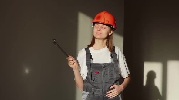 Portrait of young smiling woman engineer or builder in helmet and jumpsuit working on factory 