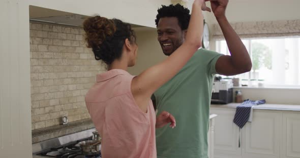 Happy biracial couple dancing together in kitchen alt