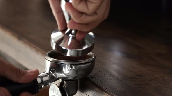 Barista pressing temper on portafilter at the table preparing to make coffee with machine