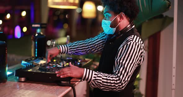 Black Dj playing music at cocktail bar outdoor while wearing face safety mask alt