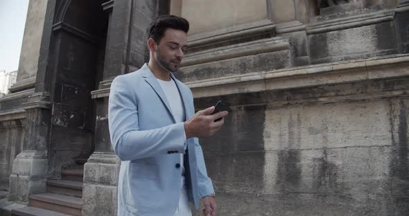 Young Man Reads An SMS On The Phone While Walking Around The City alt