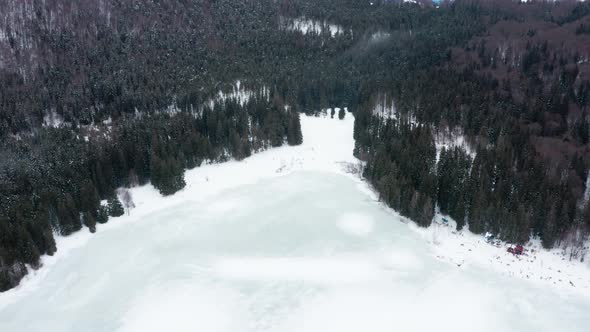 Isolated frozen volcanic crater lake in forest, Sfanta Ana, Romania, drone tilt down alt