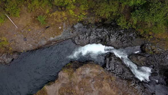 Aerial overhead footage of river flowing through rocky terrain in the forest. alt