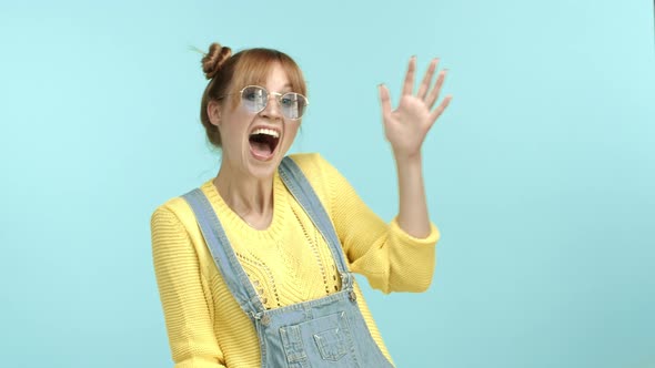 Funky Caucasian Girl with Buns Hairstyle and Sunglasses Standing in Coloful Clothes and Waving Hand