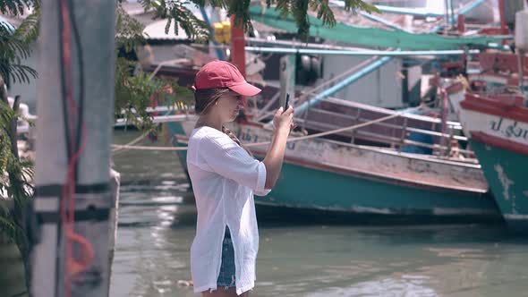 Attractive Girl in Cap Holds Cellphone Against Fishing Boats alt