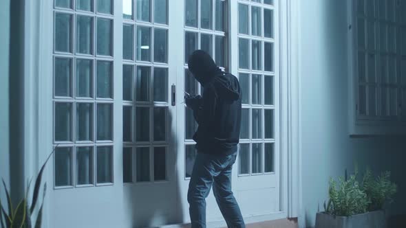 Thief Man Holding Flashlight And Looking Inside The House Before Trying To Open The Door alt