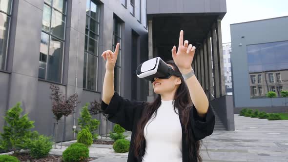 Smiling Confident Young Asian Woman in Virtual Reality Headset Working on Imaginary Screen Outdoors alt