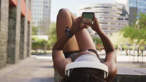 African american woman exercising outdoors wearing wireless headphone using smartphone in the city alt