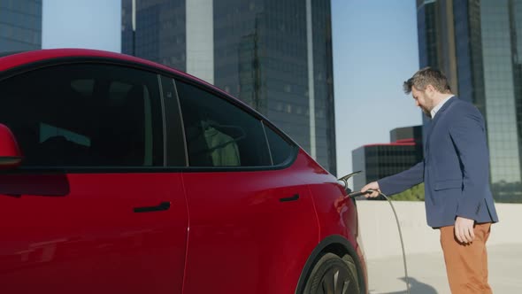 Businessman Using Smart Phone Waiting Power Supply Connected Electric Vehicle alt