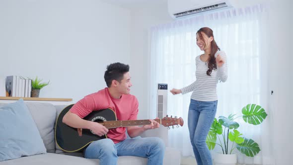 Asian young loving couple play guitar together in living room at home. alt
