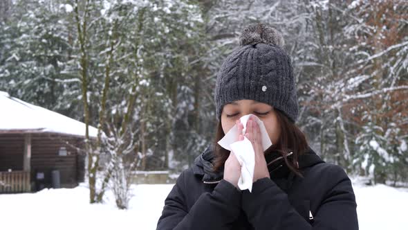 Young asian woman blows her nose in cold winter forrest in Switzerland. alt