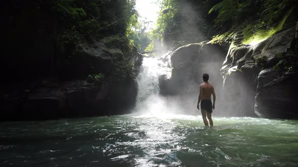 Happy Man Standing in Front of a Waterfall Feeling Free and Takes a Breathe alt