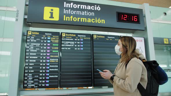 Female Traveller Wearing Medical Face Mask Hand Use Smartphone Checking Flight Schedule Standing alt