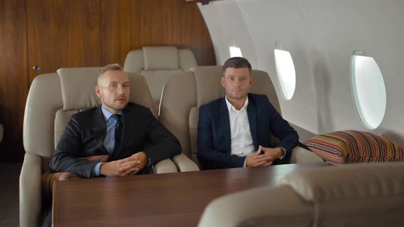 Young Businessmen Talk, Sit in Airplane Interior During Flight. alt