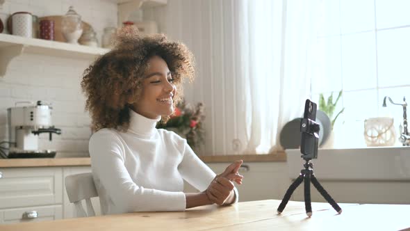 Cute Sociable African Girl Blogger Writes Her Video Blog Sitting at Home in the Kitchen on a Mobile alt