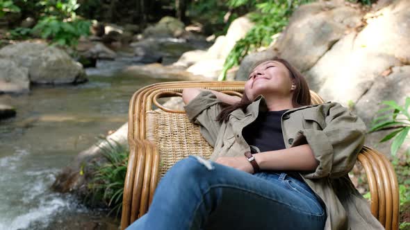 A woman lying and relaxing on wooden couch by waterfall stream