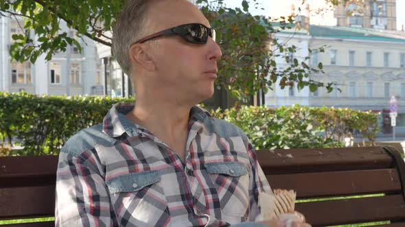 Caucasian Middle-aged Man in Sunglasses Eating Large Sandwich on Bench on Bench alt
