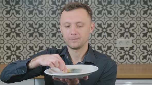 in the Kitchen a Man Takes Spoiled Cheese with Mold Carefully Examines a Piece and with Contempt