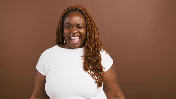 Playful African American Lady Dancing Gesturing Peace Sign Near Eyes and Winking Brown Background alt