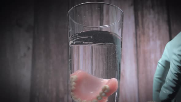 Closeup Shot of Prosthesis Teeth Being Dropped Into a Glass of Water