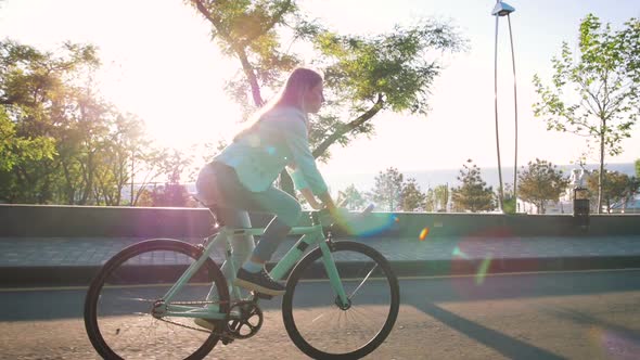 Young Stylish Woman Cyclist Enjoying Fixed Gear Bike Riding Outdoors at Sunrise Near the Sea alt