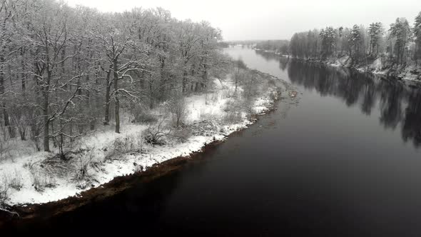 Aerial View of Frozen Trees Standing on the Bank of a Cold River in Winter alt
