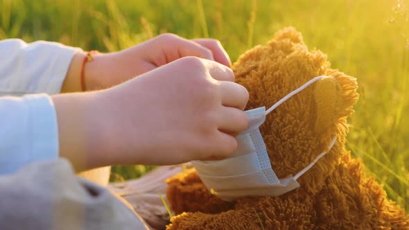 Children's Hands Put on a Protective Mask on the Teddy Bear alt