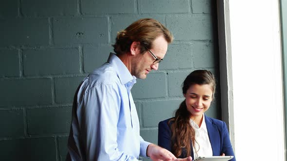 Businessman discussing with businesswoman over digital tablet alt