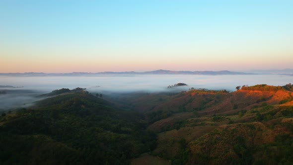 4K aerial view over mountain at sunrise in heavy fog. golden morning sunlight alt