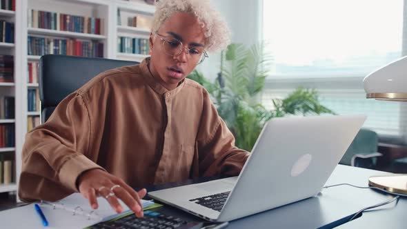Young African American Woman Counts on Calculator and Keeps Home Accounting alt